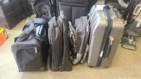 Silver hard-sided carry-on and soft-sided backpacks arranged standing upright showing size and wheels