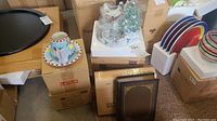 Overview of the lot showing stacked boxes with the music box, candle covers including a glass Christmas tree and a teacup, and two brown book-shaped storage boxes.