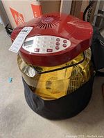 Front view of red Nuwave Pro Plus infrared oven with digital control panel and transparent glass bowl sitting on black fabric carrying base.