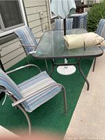 Four metal patio chairs with woven seats and striped cushions around a glass outdoor table