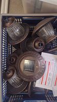 View of several brown metal and glass solar yard light covers stacked in a box with some instruction sheets.