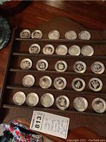 Wooden rack holding 26 round sterling silver medallions arranged in rows