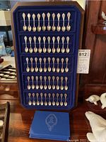 Full view of 50 miniature spoons arranged in original blue velvet‐lined display case with certificates booklet beneath