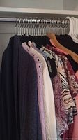 Photo of 17 women's clothing items on hangers including sweaters, blouses, and vests in various colors and patterns.