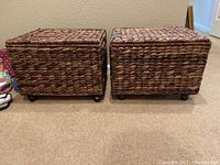 Two woven file boxes side by side on carpet, showing front and side views. Both boxes have casters and hinged lids.