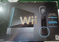 Photo of the front of the box showing the black Nintendo Wii console, black Wii Remote with MotionPlus, and the Wii Sports and Wii Sports Resort game inclusions.
