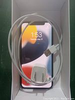 Front view of Apple iPhone X 64GB Silver with powered on display, Lightning cable and USB power adapter