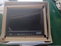 Front view of Neewer LCD Field Monitor in box with control buttons visible.