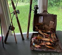 Photo of multiple vintage fishing rods and a vintage carrying box filled with antique handmade wooden fishing lures.