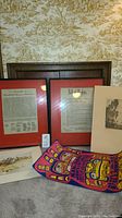 Framed Bill of Rights and Declaration of Independence prints with red-orange matting, and other prints including Native American themed colorful print and black and white sketch.