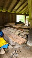 Wide view of stacked wood lumber and tarps inside barn corner