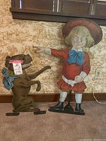 Front view of both Buster Brown and Tige metal signs side by side on stands against wall