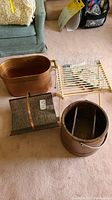 View of the copper tub, rectangular copper tray, wooden bucket, and white metal rack arranged on carpet.