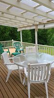 White patio set with round glass-top table and four white chairs on wooden deck under pergola