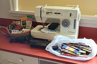 Front view of Singer Merrill sewing machine with bag of assorted sewing notions and scissors on red countertop.