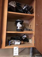 Power tools including router with bits, jigsaw, and Skilsaw circular saw inside a cabinet.