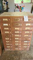 Front view showing 30 small numbered drawers with metal label holders in the wooden cabinet.
