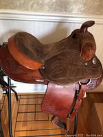Side view of the tooled leather show saddle placed on the black metal saddle stand showing detailed tooling and suede seat.