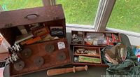 Overview photo of wooden tackle box opened showing reels, boxes of hooks, and tackle inside