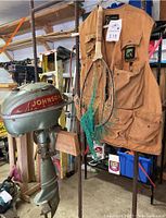 Full view of the Johnson SeaHorse outboard motor, fishing vest hanging alongside a fishing net with wooden handle, items located in garage setting