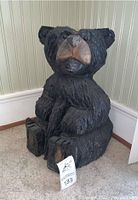 Front view of wooden black bear statue showing carved details on face, paws, and body.