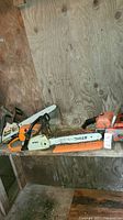 Two chainsaws on wooden shelf: green Craftsman 16" 36cc and Stihl with bar cover
