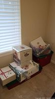 Photo showing stacked storage bins and boxes for Christmas decorations in a corner of a room with a window and closed blinds.