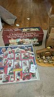 Photo showing boxed Original Classics Moving Musical Holiday Train, set of wooden Santa Claus ornaments, and the wooden nativity figurines arranged on floor.