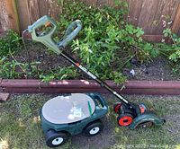 Black & Decker Edge Hog electric garden edger alongside green plastic garden cart with beige seat lid on grass near a wooden border and plants.