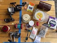 Overview of lot with five fishing reels, assorted fishline, sinkers, shafting beads, stringers, and other gear scattered on a wooden table.