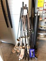 Photo showing an assortment of golf clubs mostly with wooden shafts and fabric or furry club head covers, along with a black cylindrical putter holder and blue pack of golf balls