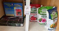 Shows Topsy Turvy Hummingbird Hangout Planter box, multiple bags of Expert Gardener organic fertilizers including Vegetable & Tomato Food, All-Purpose Plant Food, and Flower Food in colorful printed bags.