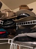 Shelf of assorted hats including camouflage, straw, felt, and black tiara style hat. Folded shirts below.