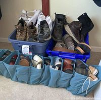 Plastic bins and shoe organizer filled with various men's shoes including hiking boots, athletic shoes, leather boots, and sandals, showing collection and condition