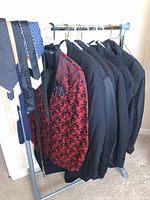 Six men's formal jackets hanging on a rack with six ties hanging on the side of the rack, including one red-black floral pattern jacket.