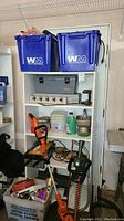 Wide view of shelving with blue tubs, garden tools, and miscellaneous items