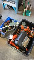 Blue bins filled with multiple power tools including drills, a hedge trimmer, saws, black carrying cases, and many power cords and chargers scattered inside.