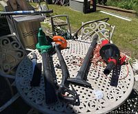 Outdoor metal table with garden tools placed on top including leaf blower and weed wacker.