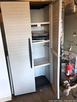Photo showing storage cabinet open with three shelves and photo albums inside, doors partially open.