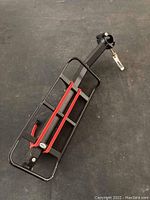 Black metal bike rack with red bungee cords laid flat showing adjustable clamp for mounting.