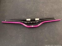 Photo showing three bike handle bars arranged horizontally, one pink Renthal brand and two black V2 brand bars.