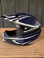 Side view of a blue, black, and white Fox dirt bike helmet showing Fox logo and curved striping design.