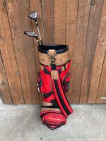 Full view of the red and tan Cypress golf bag standing upright with two clubs inside