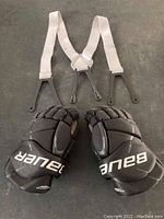 Top view of Bauer Vapor 12Palms hockey gloves and white elastic suspender laid flat on surface