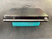 Front view of the black LG DVD player showing the disc tray, control buttons, and volume knob.