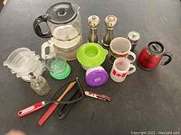 Various household kitchen and dining items including glass coffee maker, thermal carafe, mugs and cups, salt and pepper shakers, kitchen scale and utensils.
