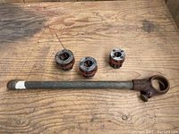 Rigid pipe threader handle and three threading dies on wooden table