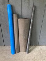 Four assorted rolls of roofing paper leaning against a wall, showing color and size variations.