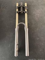 Full view of mountain bike dual crown suspension fork with gold-colored stanchions and silver lowers on dark background