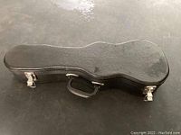 Closed black hard-shell ukulele case showing buckles, handle, and exterior texture.